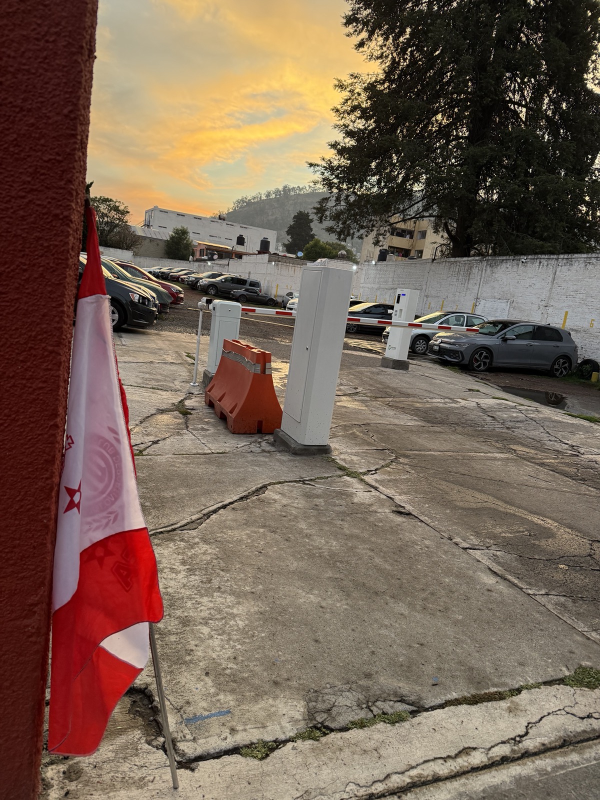 Patio del estacionamiento al atardecer con pluma automática y cajero